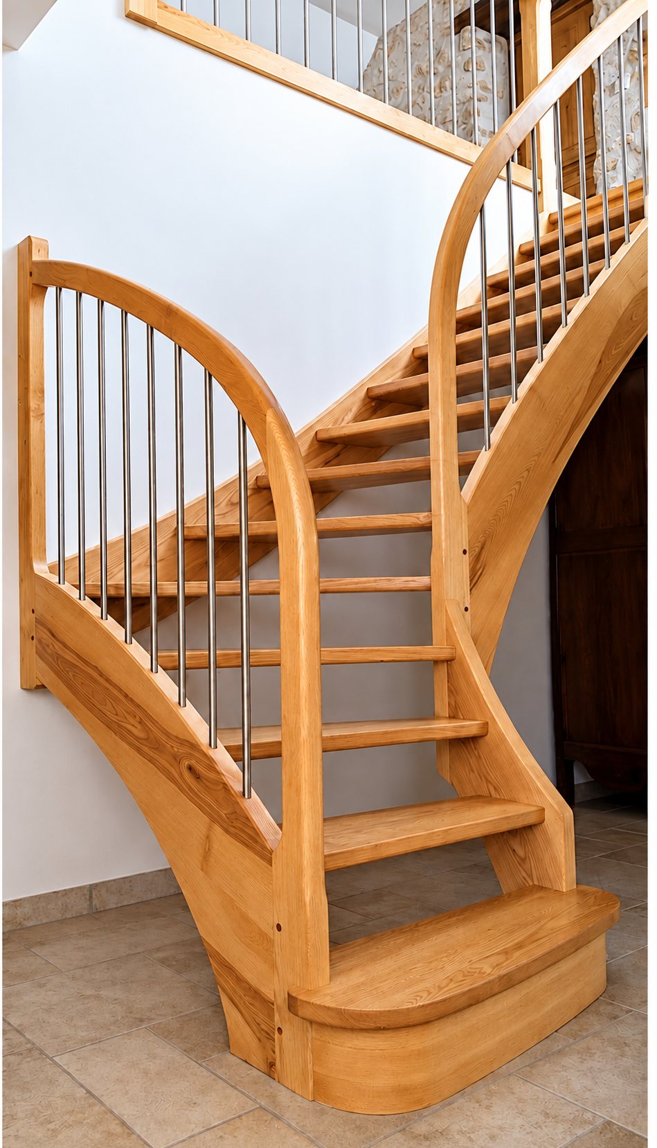 Escalier tournant en bois clair à marches ouvertes, avec rampe courbe et barreaux en métal, installé dans une maison au sol carrelé.